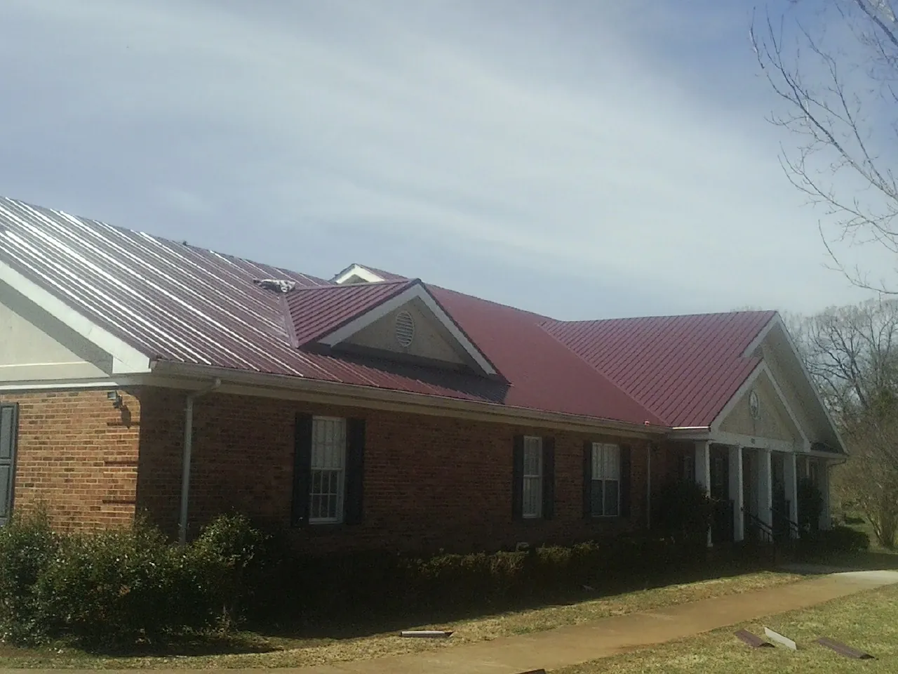 Red metal roof with gabled entries on a long brick building, from a Hail Damage Roof Repair job in Imperial