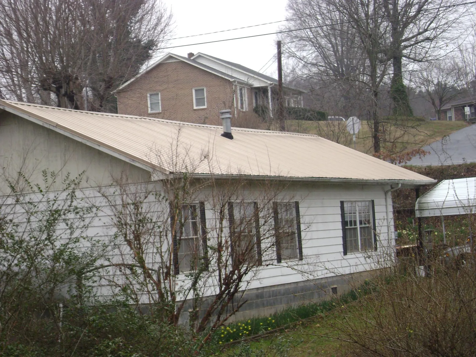 Tan metal roof on a white sided house set into a hillside — Commercial Roofing by Roofing Brothers in Imperial
